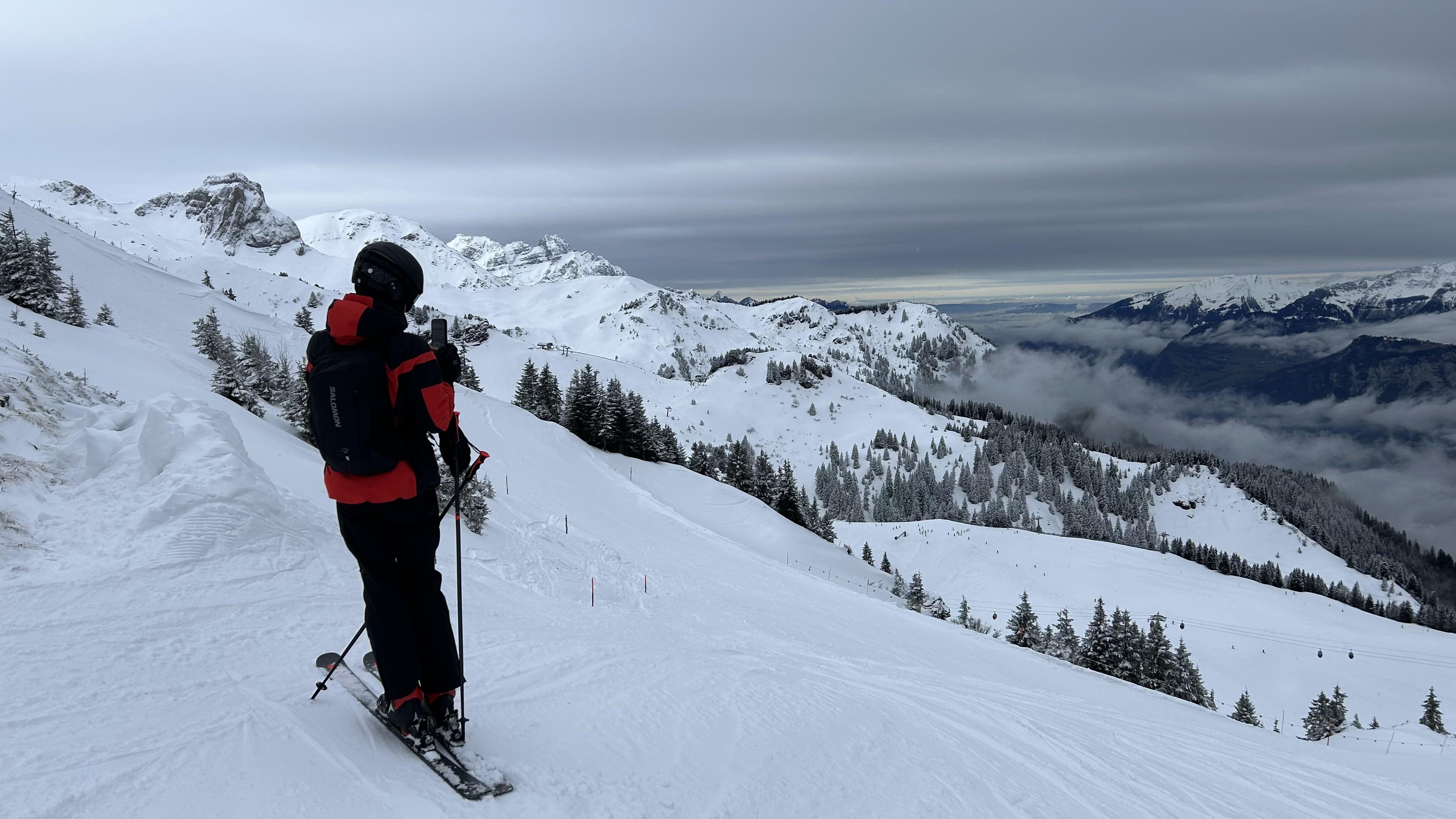 Oriol on skis at the top of a run in the Swiss Alps, looking out over cloud-covered valleys